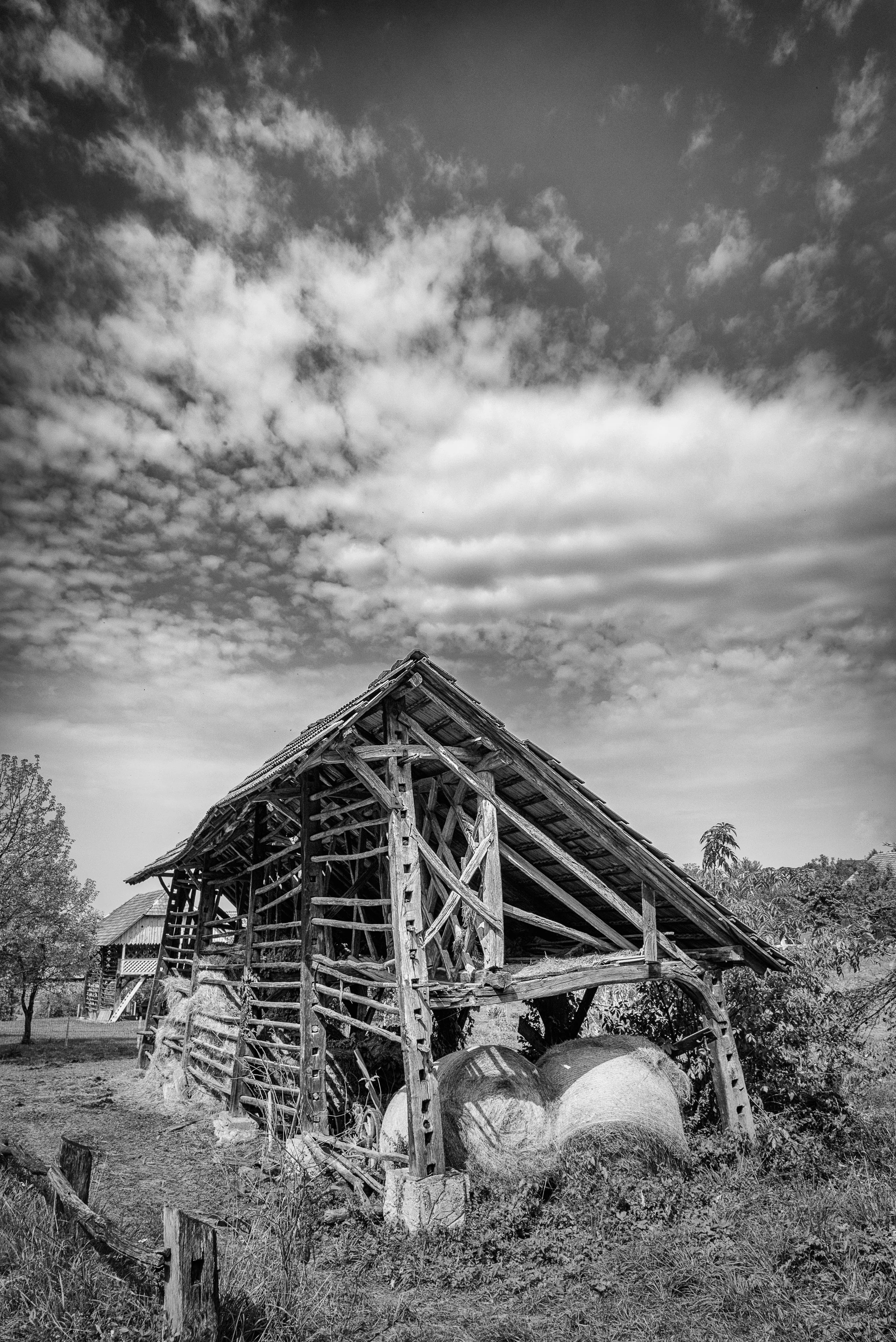 Old wooden barn in black and white with a cloudy sky in the background.