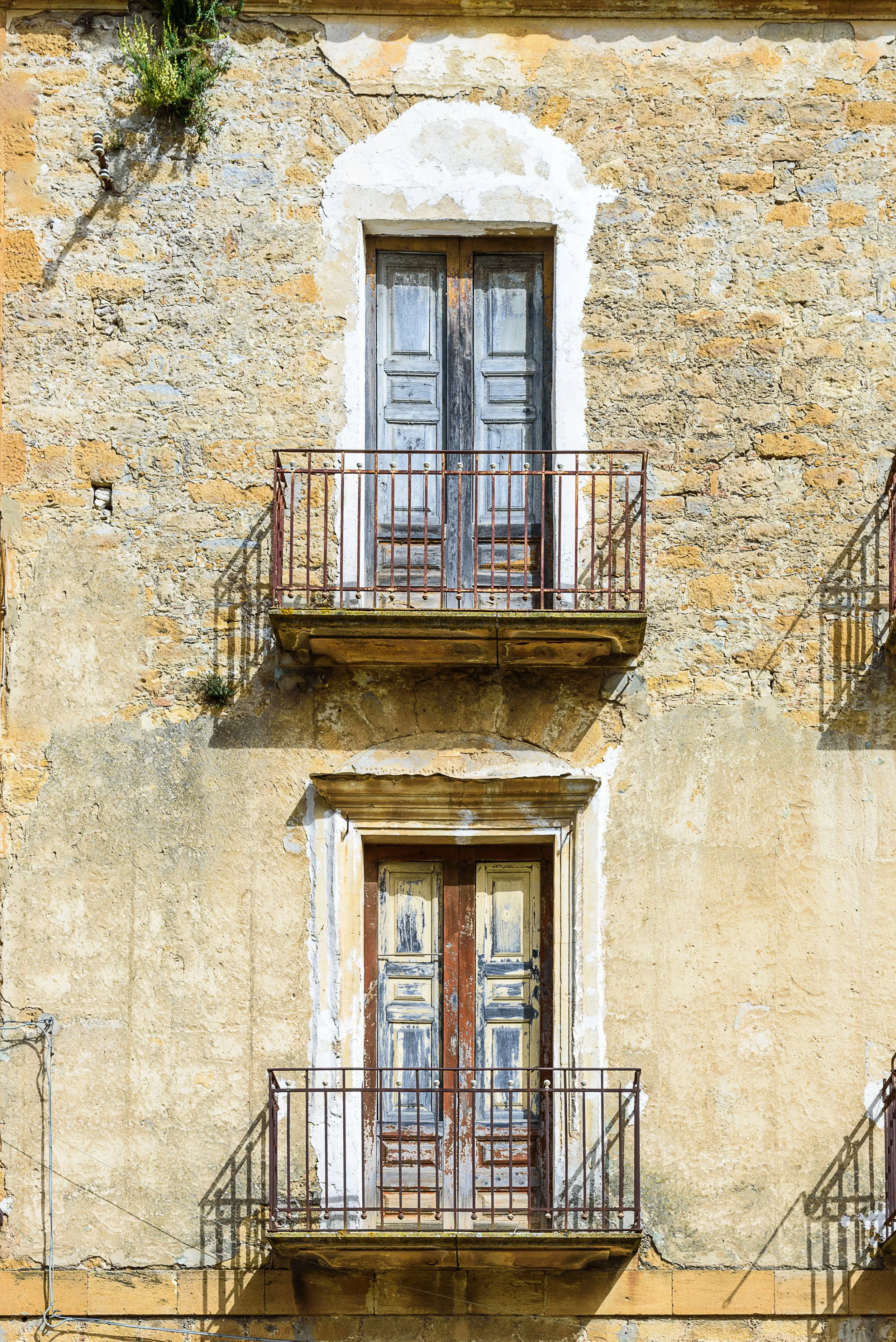 Two weathered wooden balcony doors on an old stone building with iron railings, surrounded by yellow and beige textured walls.