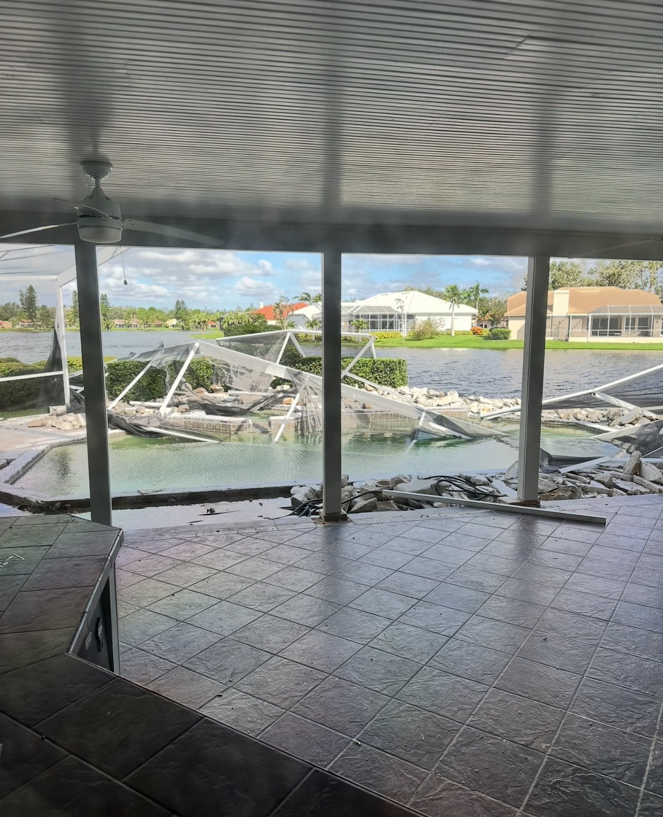 View of a screened-in porch overlooking a canal with a fallen screen and debris in the water and on the porch.
