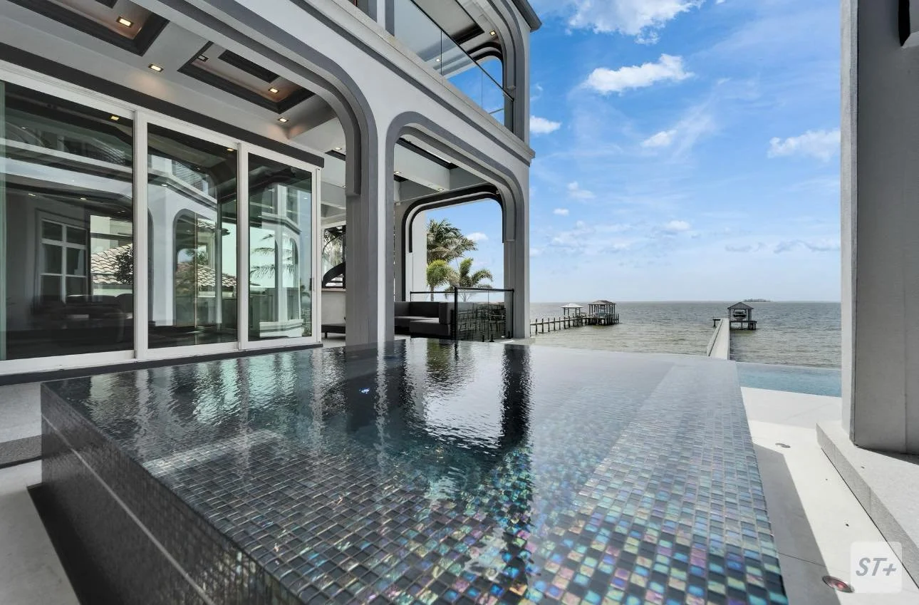 Modern beachfront house with glass doors, small pool, and ocean view with pier and overwater structures