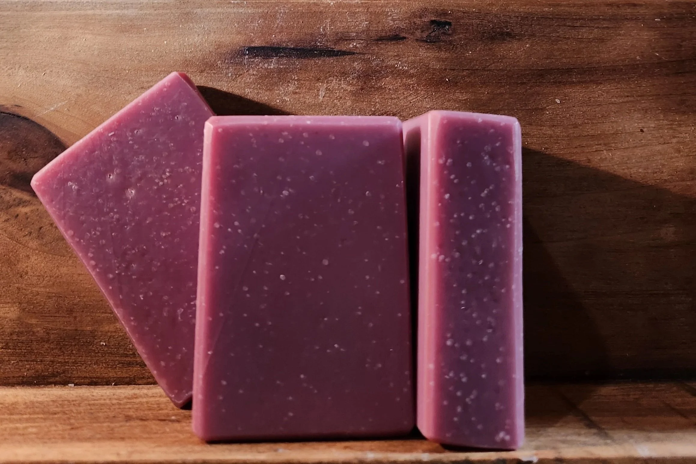 3 bars of purple soap with a wood grain background.
