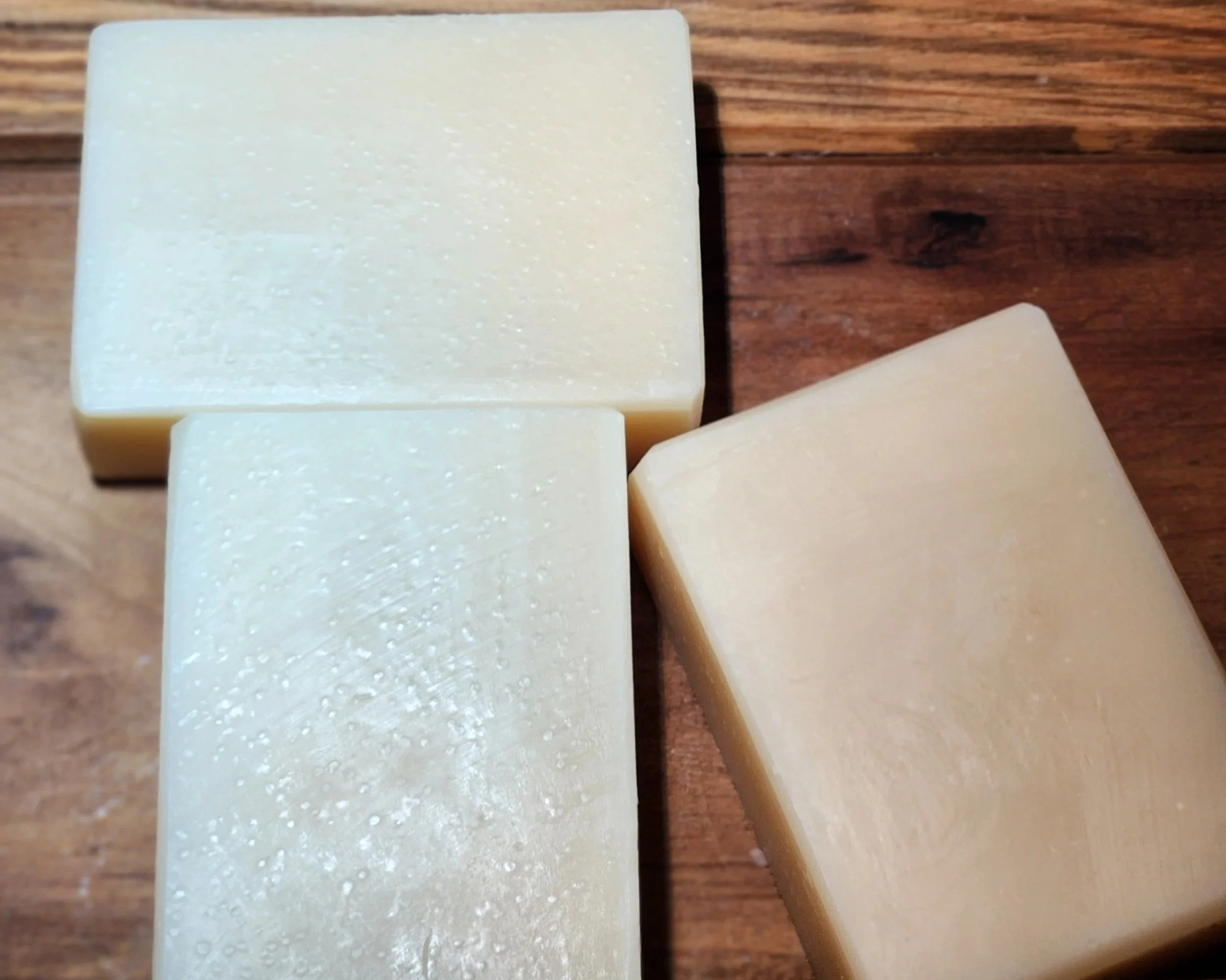 3 white bars of soap with a brown wood grain background.