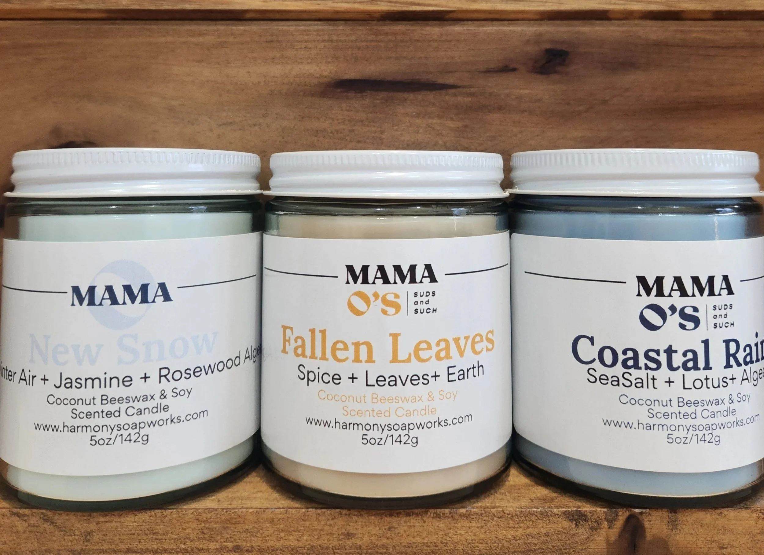 3 clear candle vessels in a row, with white metal lids.  Fragrances pictured are Fallen Leaves, New Snow and Coastal Rain.