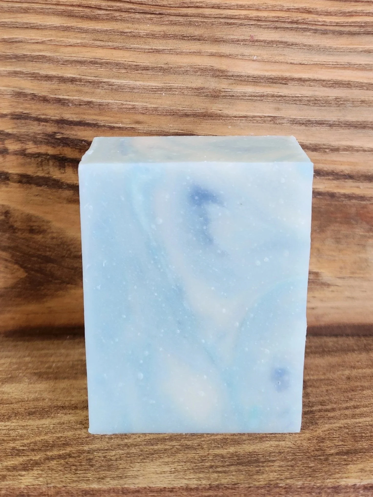 3 bars of 1 white soap bar with blue and teal swirls with a brown woodgrain background.