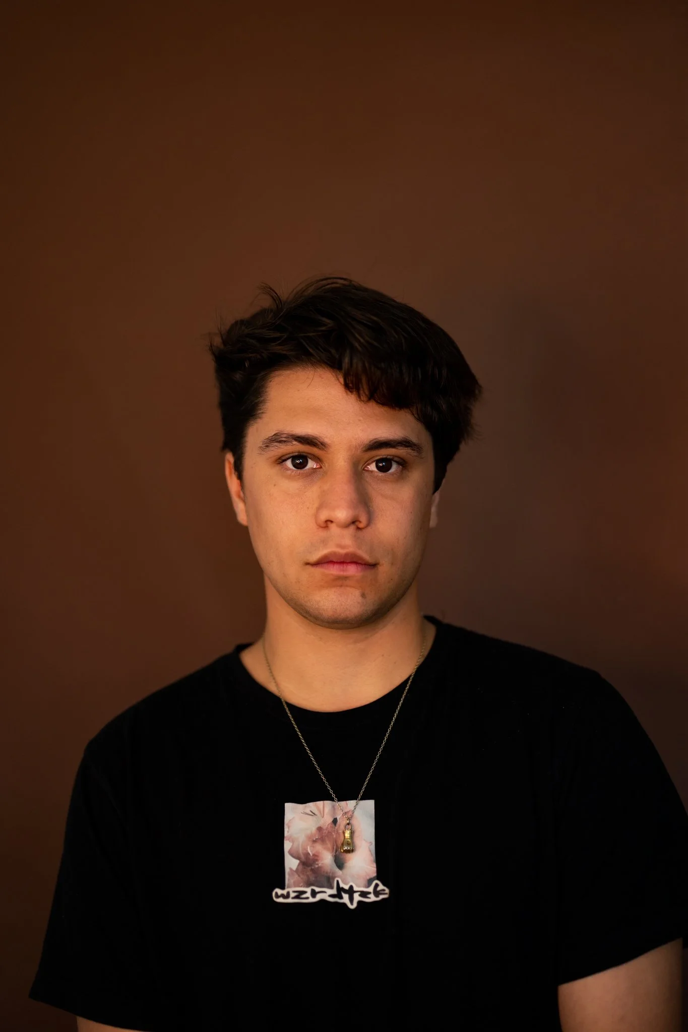A portrait of young indigenous man, posing in front of a brown wall, for a indigenous creative scholarship and magazine.