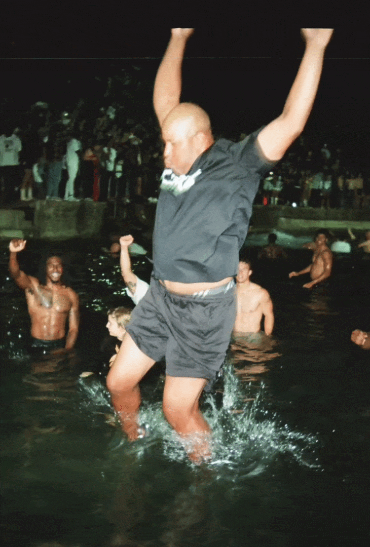 A man jumping into a body of water at night, surrounded by other people enjoying the water and celebrating.