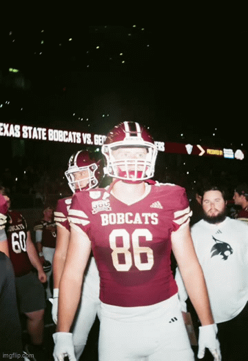 Football player wearing a maroon jersey with the number 86 and 'BOBCATS' on it, standing in a stadium with other players and staff, scoreboard showing Texas State Bobcats vs. Georgia Southern Eagles.