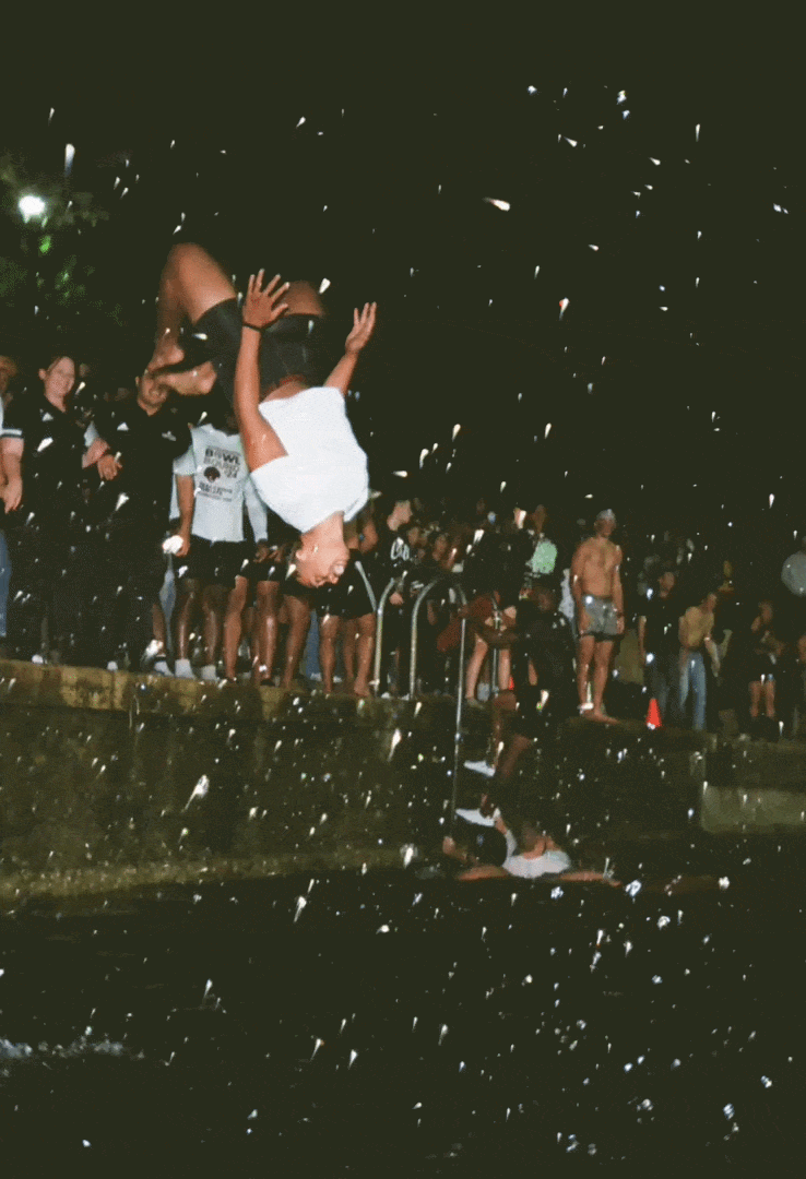 Person performing a backflip into water during night festival with onlookers.