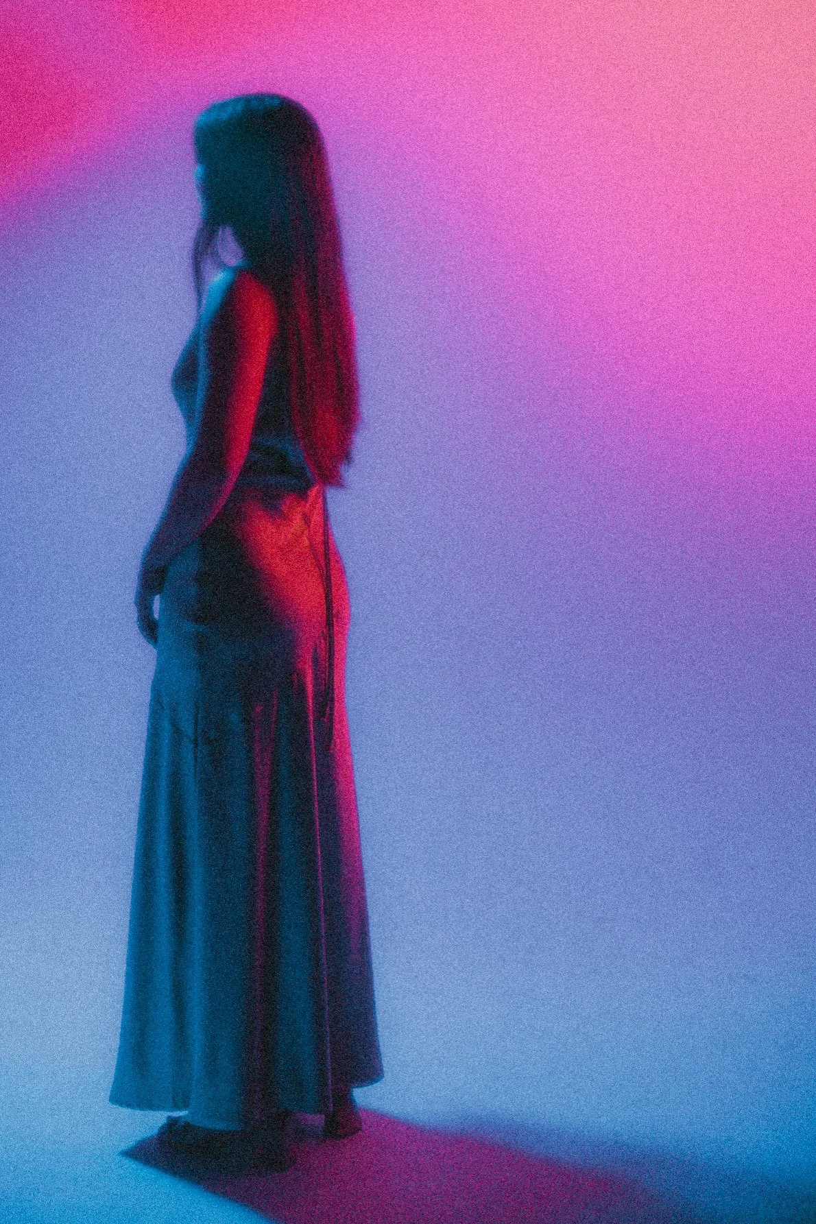 Silhouette of a woman with long hair, wearing a long dress, standing against a colorful gradient background.