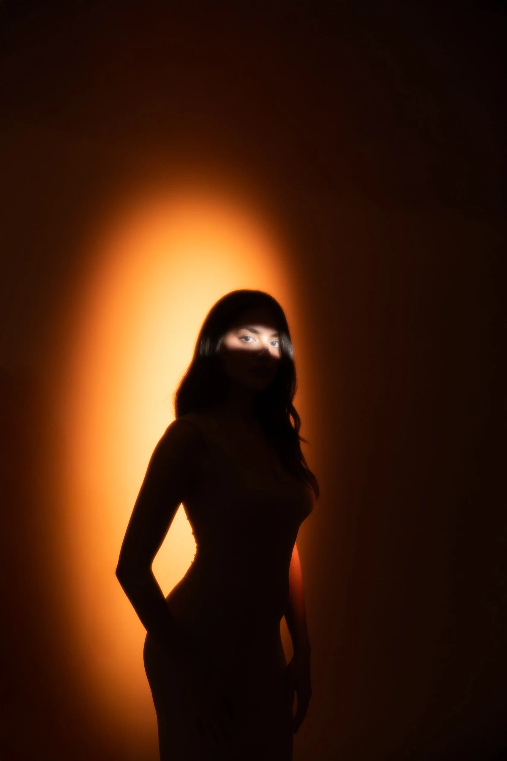 The image features a woman standing in front of an orange glowing background, casting a shadow over part of her face and body.
