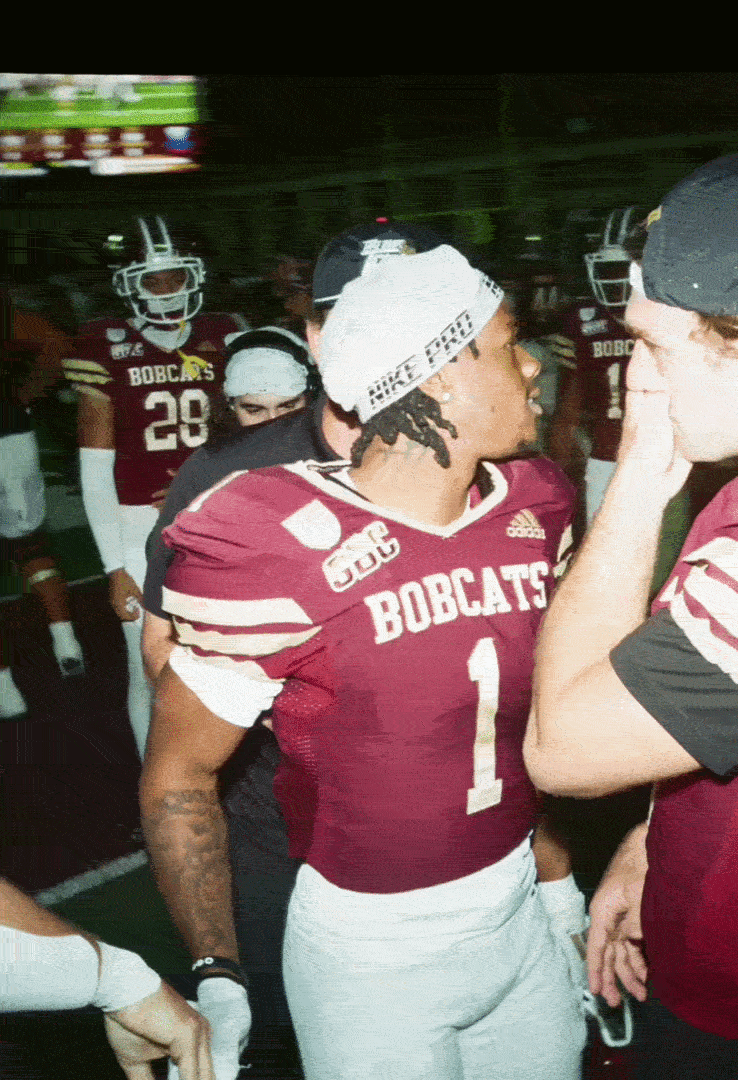 American football players from the Bobcats team in team gear, including helmets, in a sideline huddle.