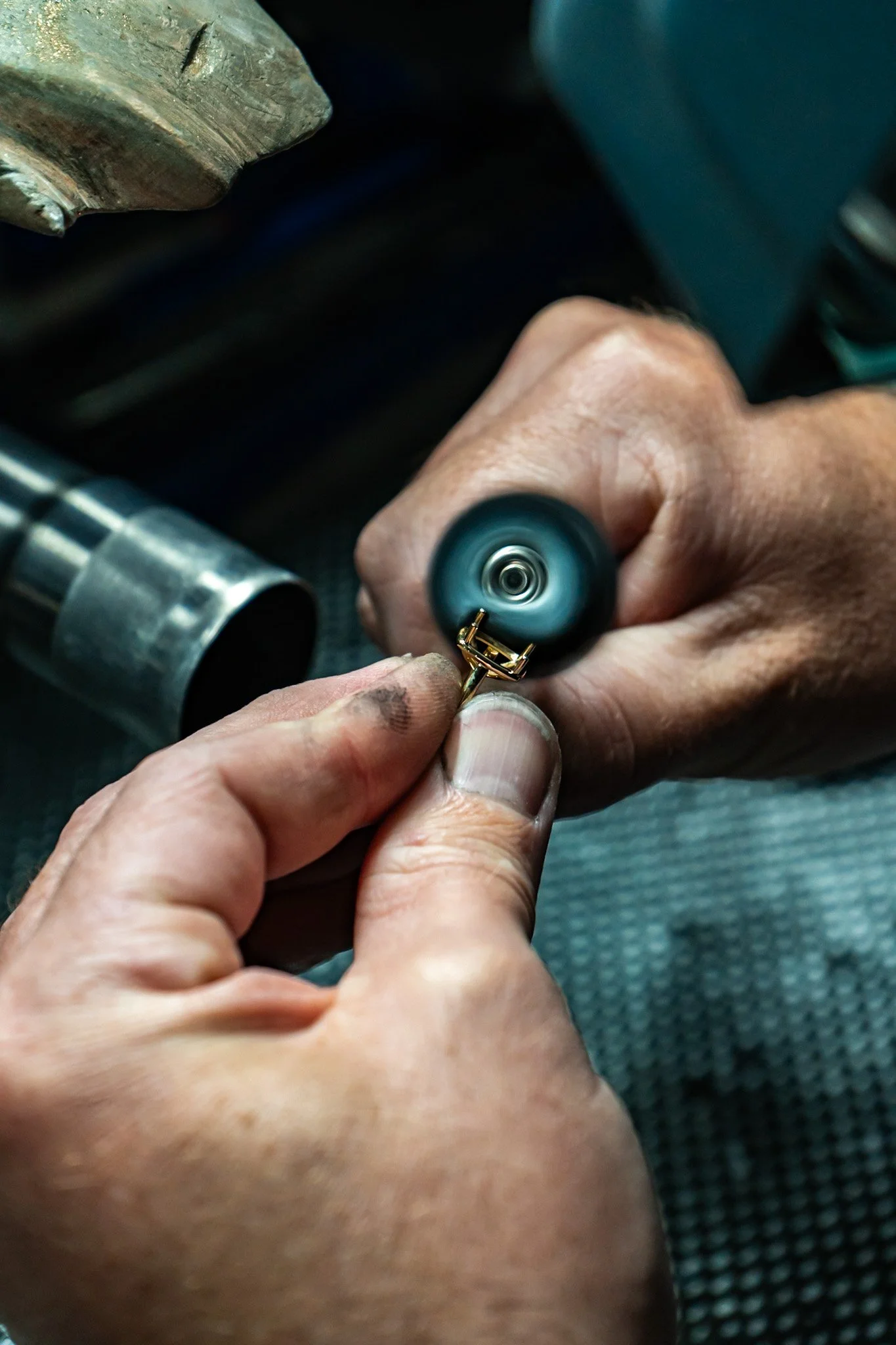 Close-up of a person holding a small screw or bolt with a power tool, working on a cylindrical metallic object that appears to be a motorcycle or machinery component.