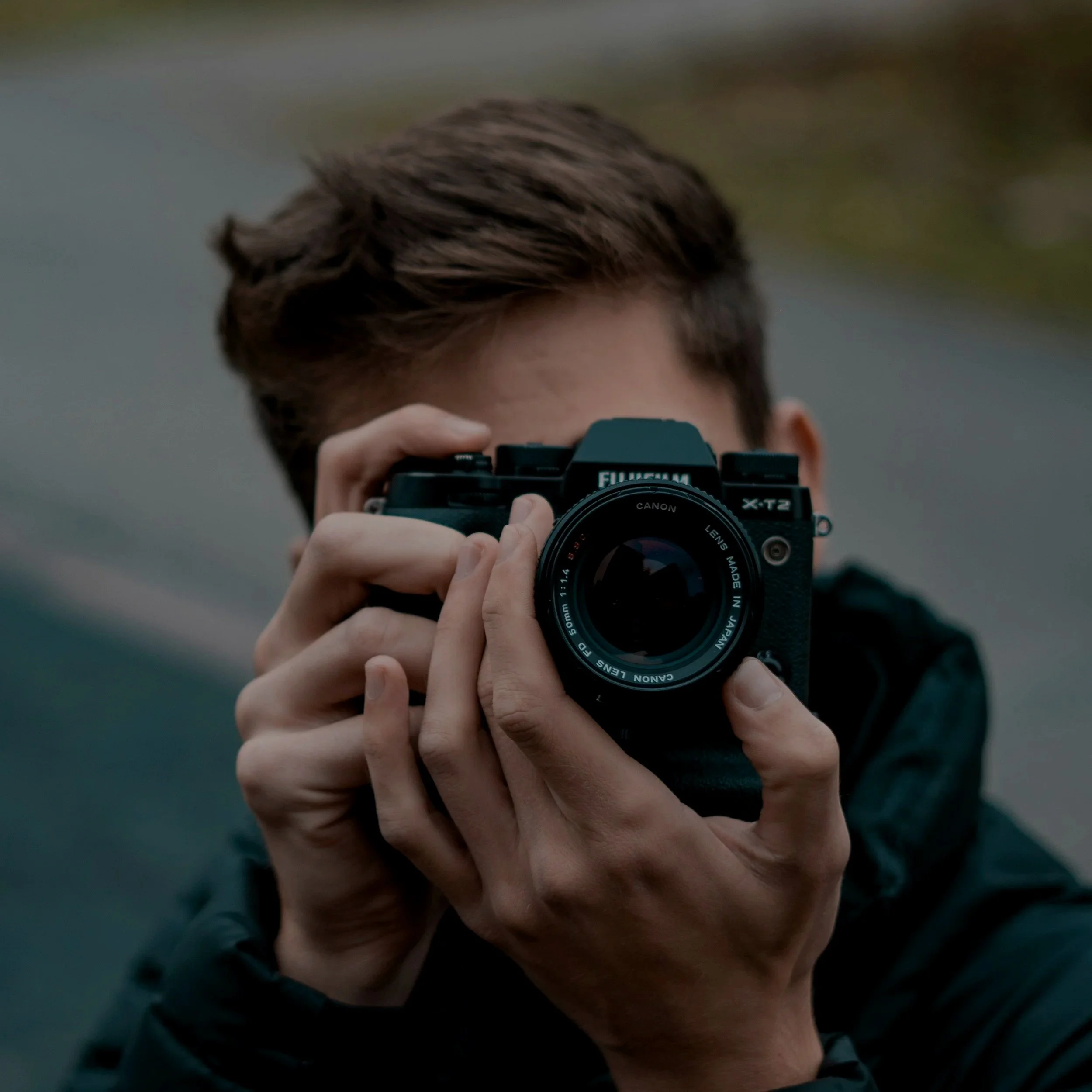 Person med brunt hår tar bilde med en svart Canon-kamera.