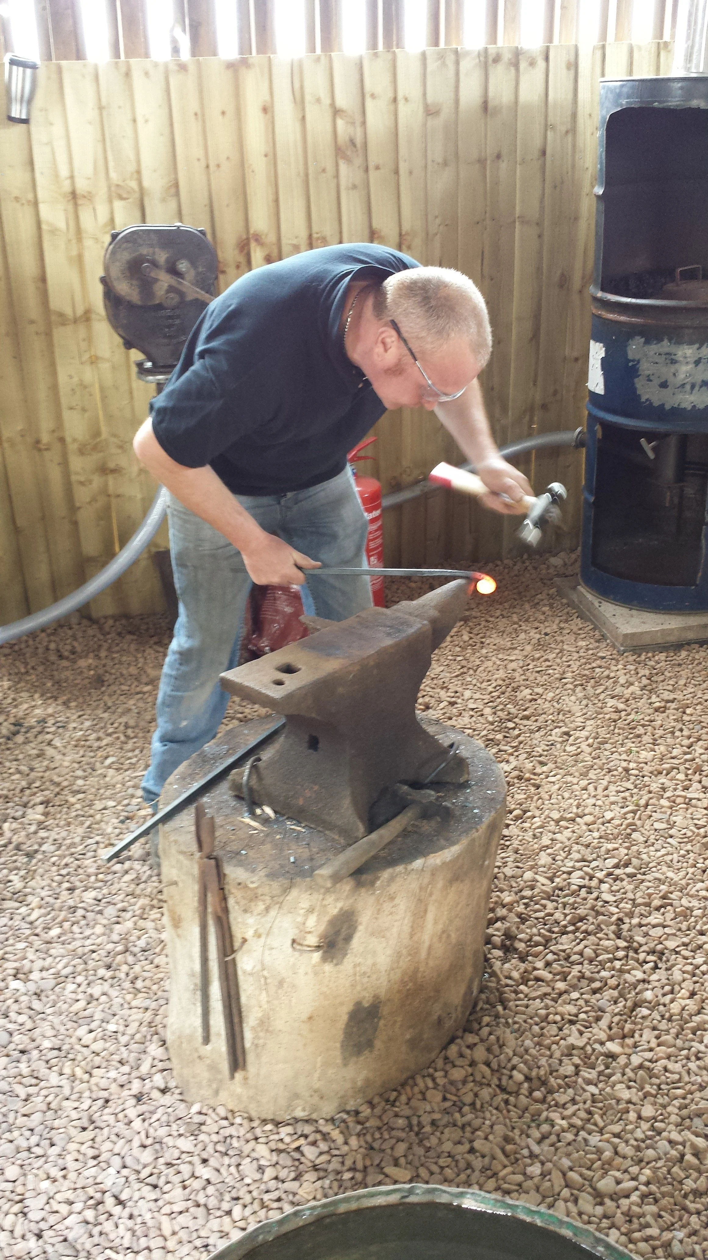 A man is working at a blacksmithing forge, heating metal with a hammer and an anvil.