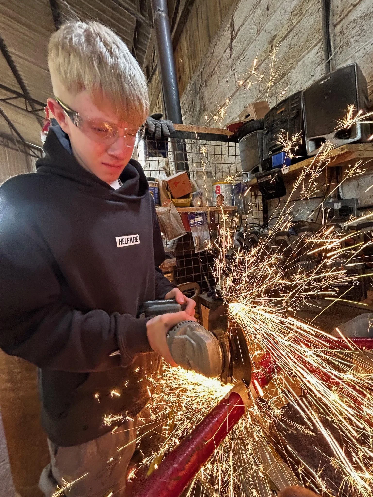 A person using an angle grinder to cut metal, creating sparks in a workshop.