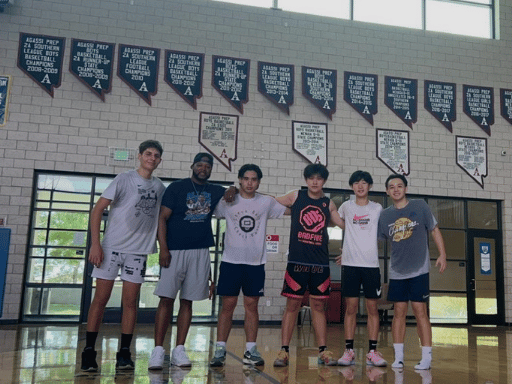 Six young men standing together in a gymnasium, posing for a photo, with banners hanging on the wall behind them.