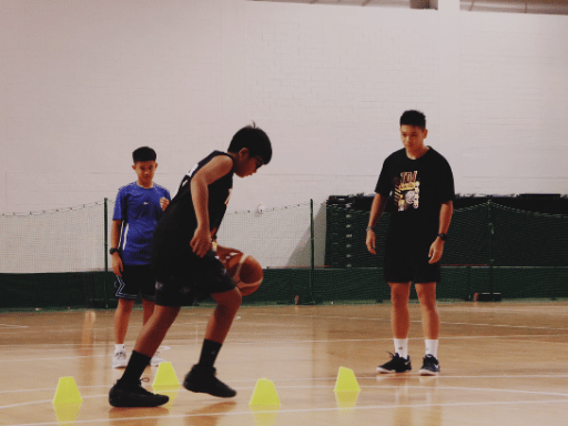 Two boys practicing basketball skills with cones on an indoor court with tdj coach