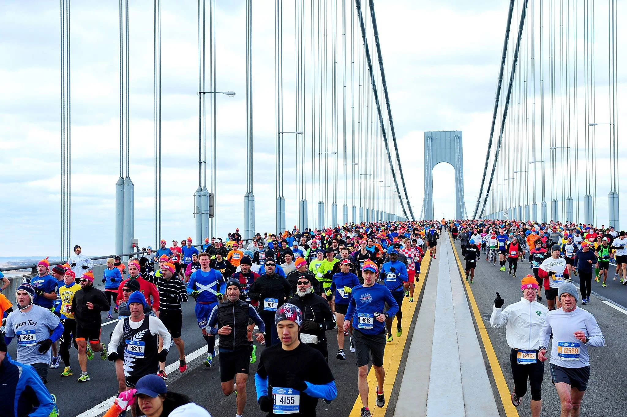 A large group of people running in a marathon on a bridge with suspension cables.