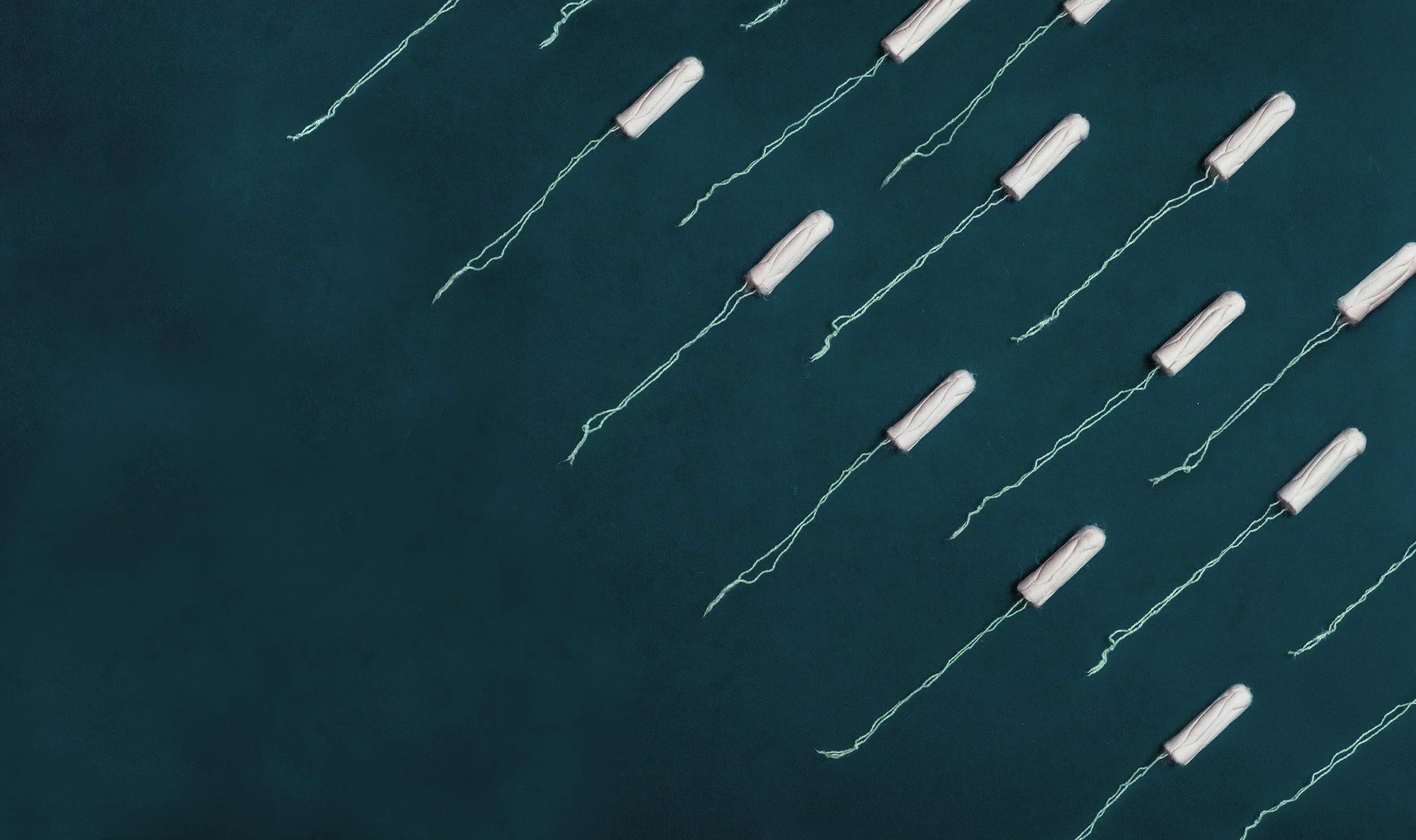 Multiple white tampons with strings on a dark teal background arranged in diagonal rows.