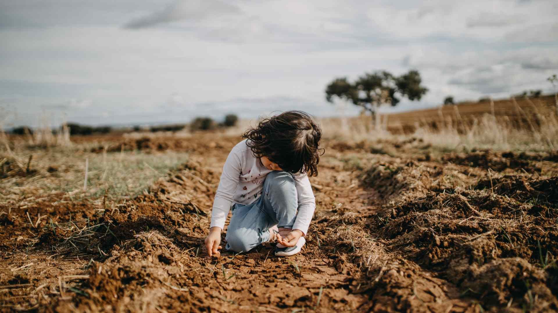 Kind sitzt auf dem Boden und spielt mit der Erde