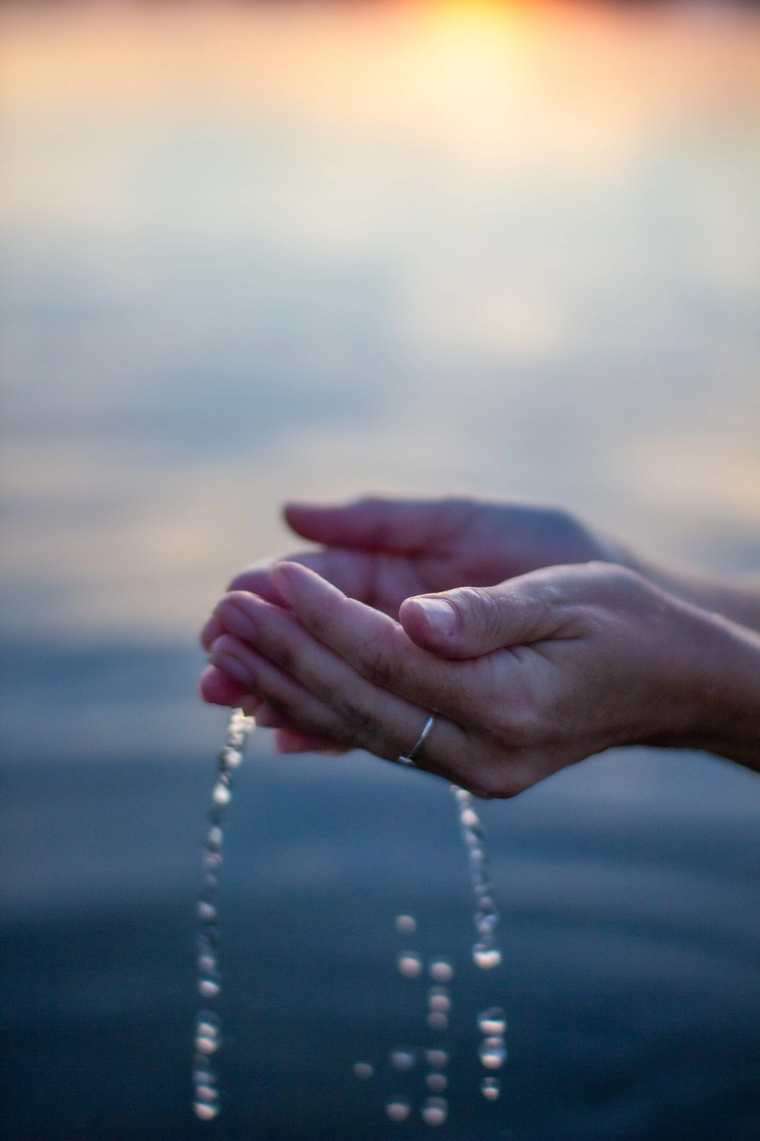 Eine Hand hält Wasser, das in den See tropft, bei Sonnenuntergang.
