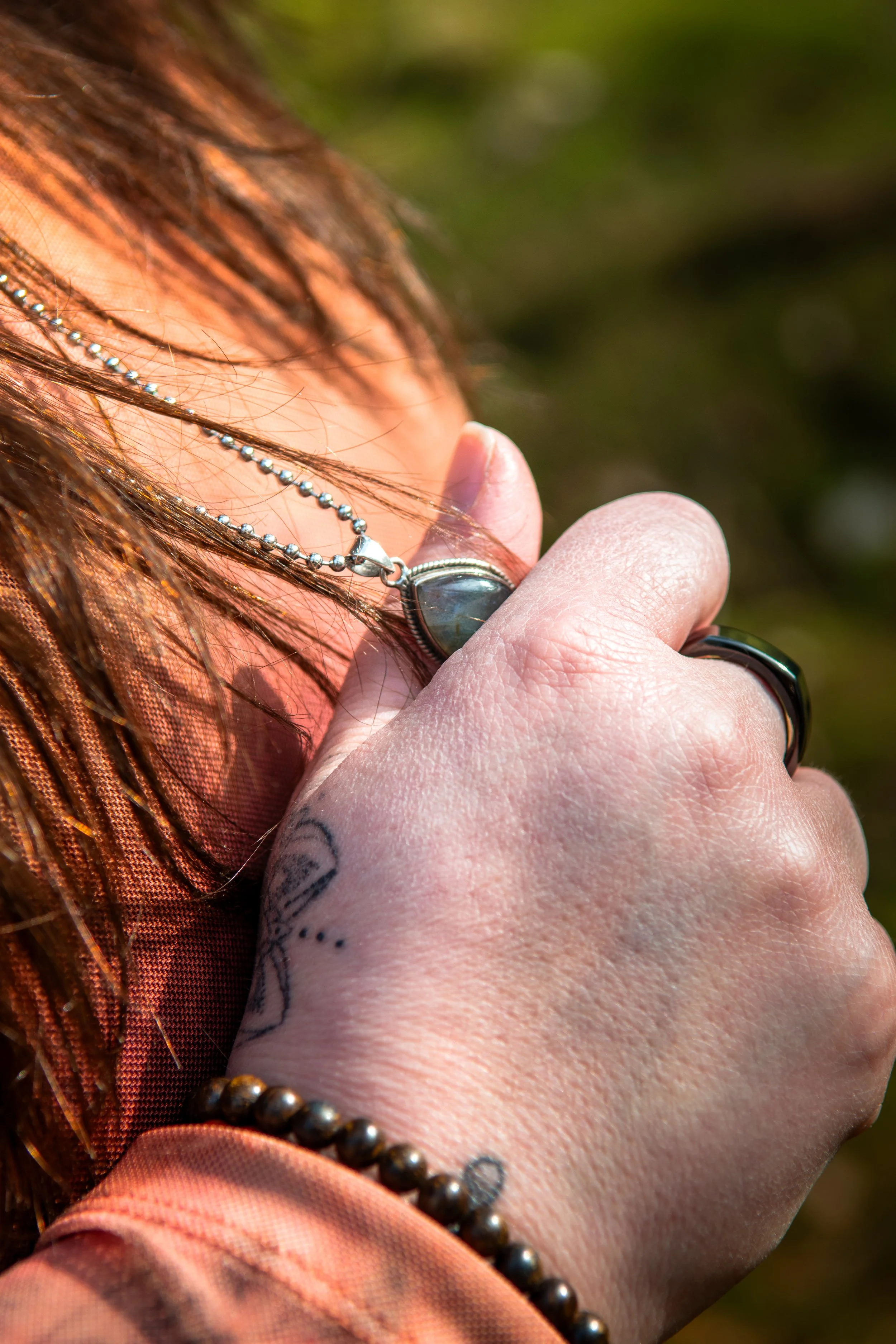 Close-up van een hand die een ketting vasthoudt, met een achtergrond van lichtgroen en bruin.