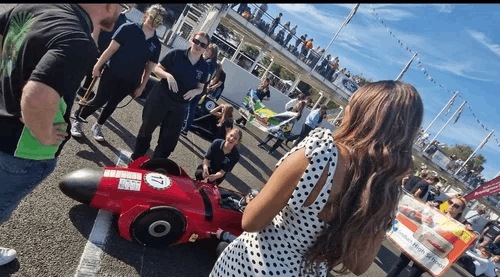  A group of people stood round a kit car on a race track 