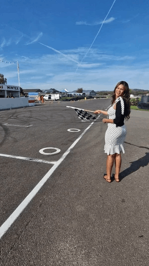  A woman stood smiling on a race track, holding a checked flag 