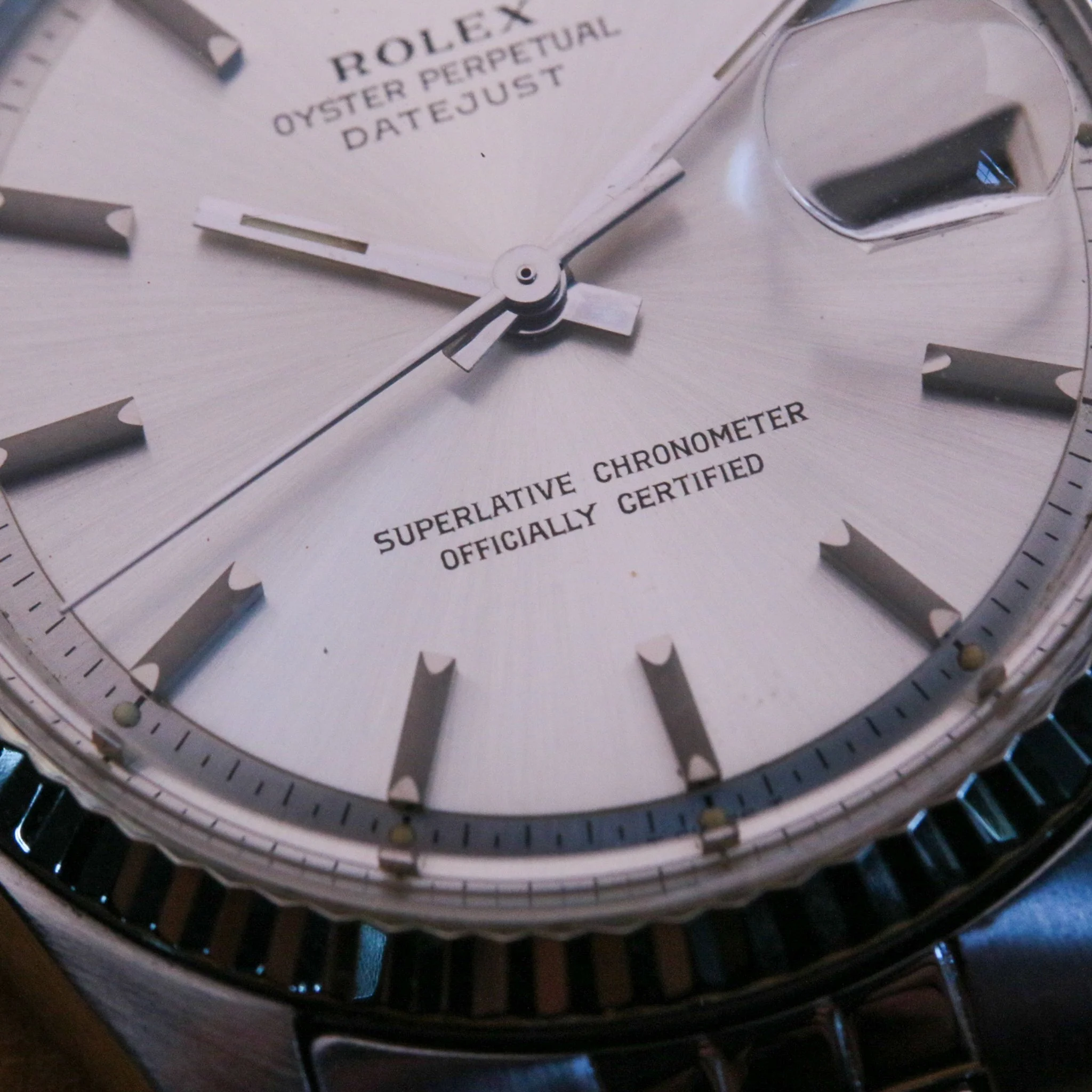 Close-up of a Rolex watch face showing hands, date, and text, with a metal bezel and black dial.