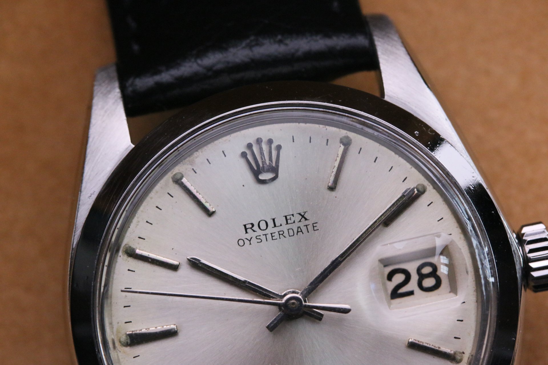 Close-up of a Rolex Oysterdate wristwatch showing the time and date, with a black leather strap.