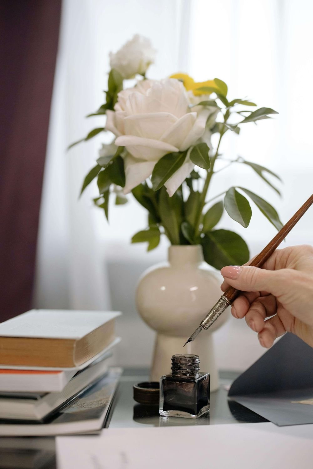 Hands preparing to dip calligraphy pen in ink beside vase of flowers – symbolizing intentionality, creativity, and the reflective process of trauma therapy for deep thinkers
