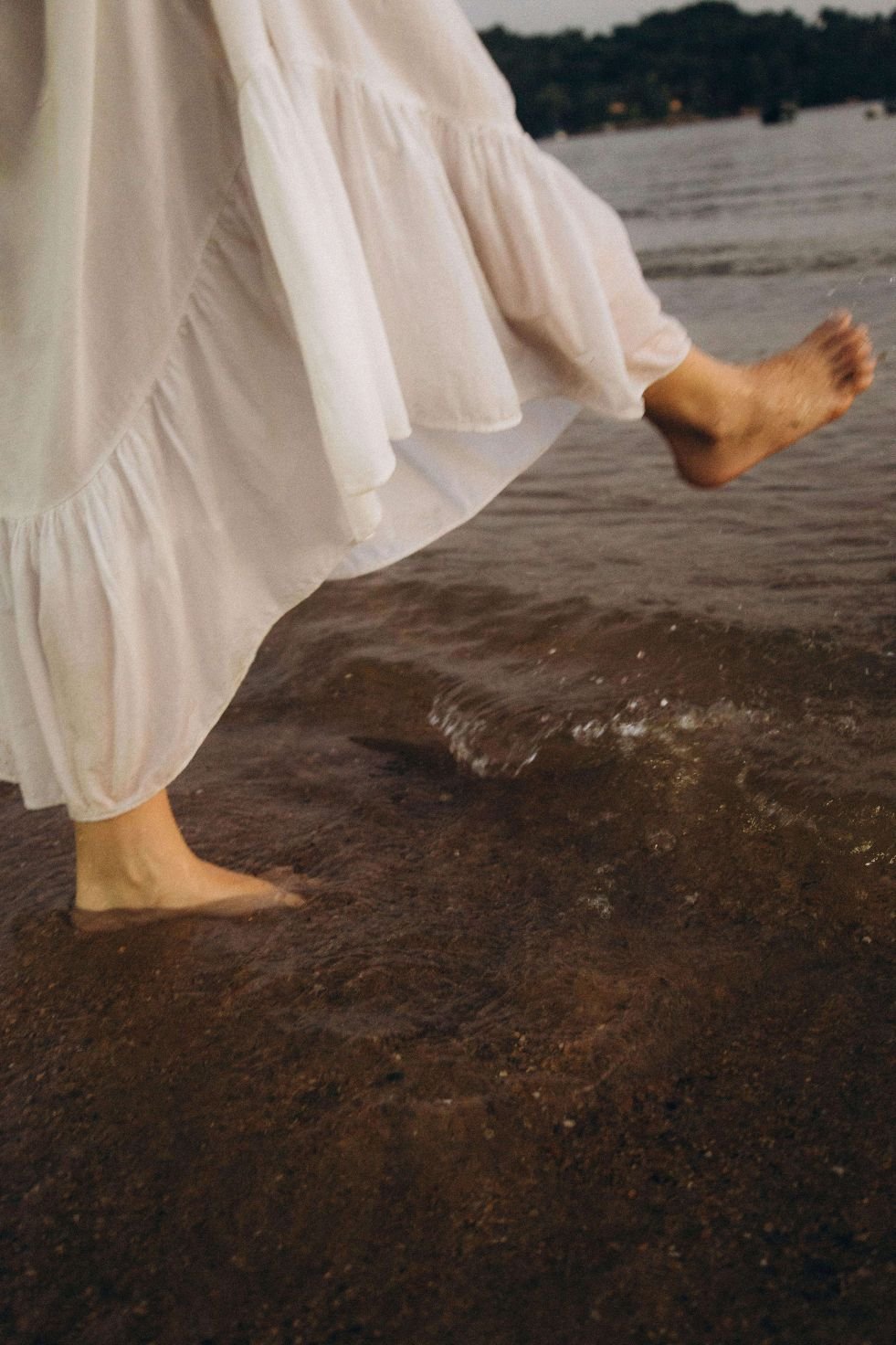 Woman in chiffon skirt stepping barefoot into ocean, embodiment and courage in trauma therapy San Antonio Texas