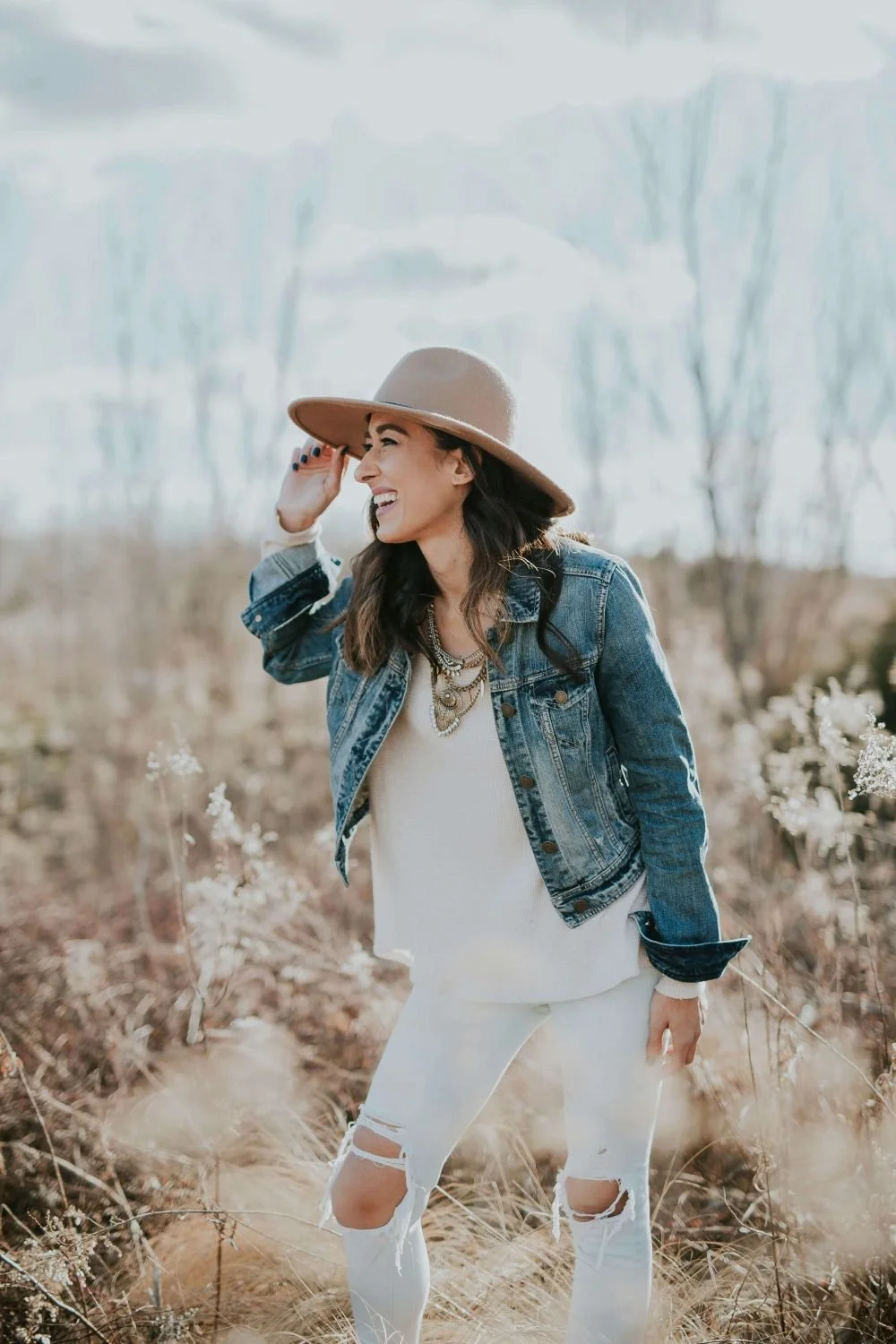 Smiling woman with hand on hat, looking to the side, representing hope and healing in online trauma and attachment therapy in Texas.