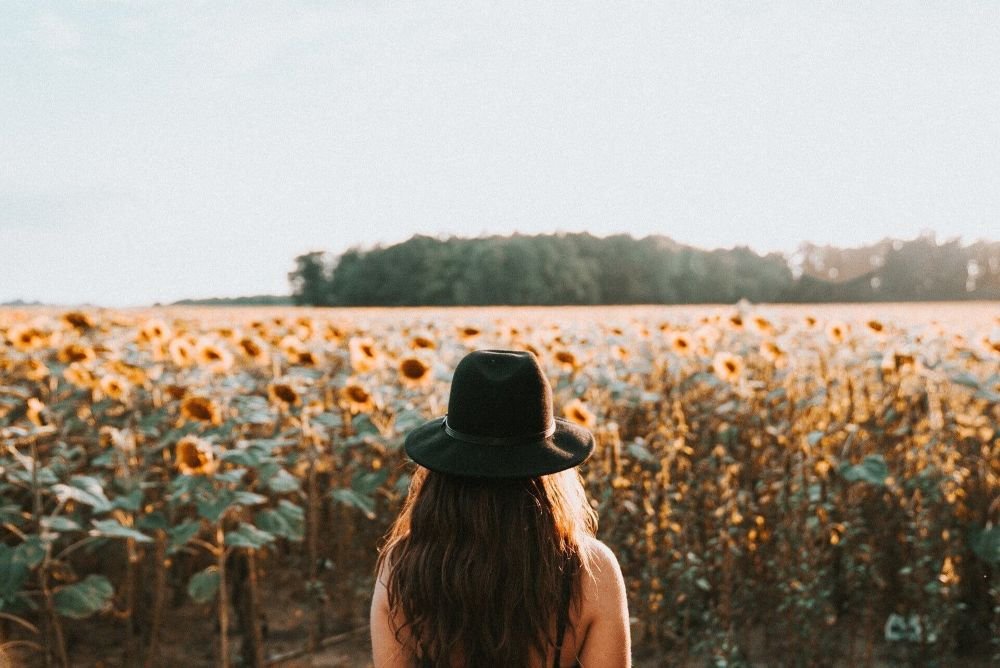 Woman in a stylish hat looking thoughtfully over a sunflower field, contact trauma therapist Rebecca Flores LPC San Antonio Texas