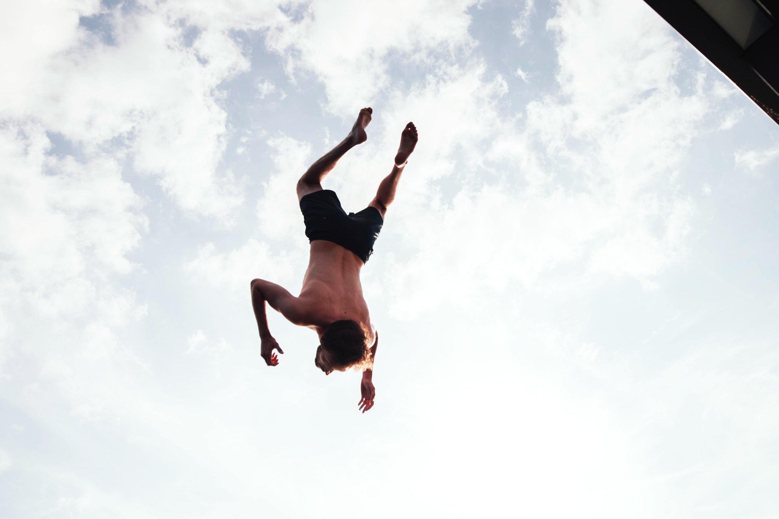 Person mid-air performing a backflip against a cloudy sky.