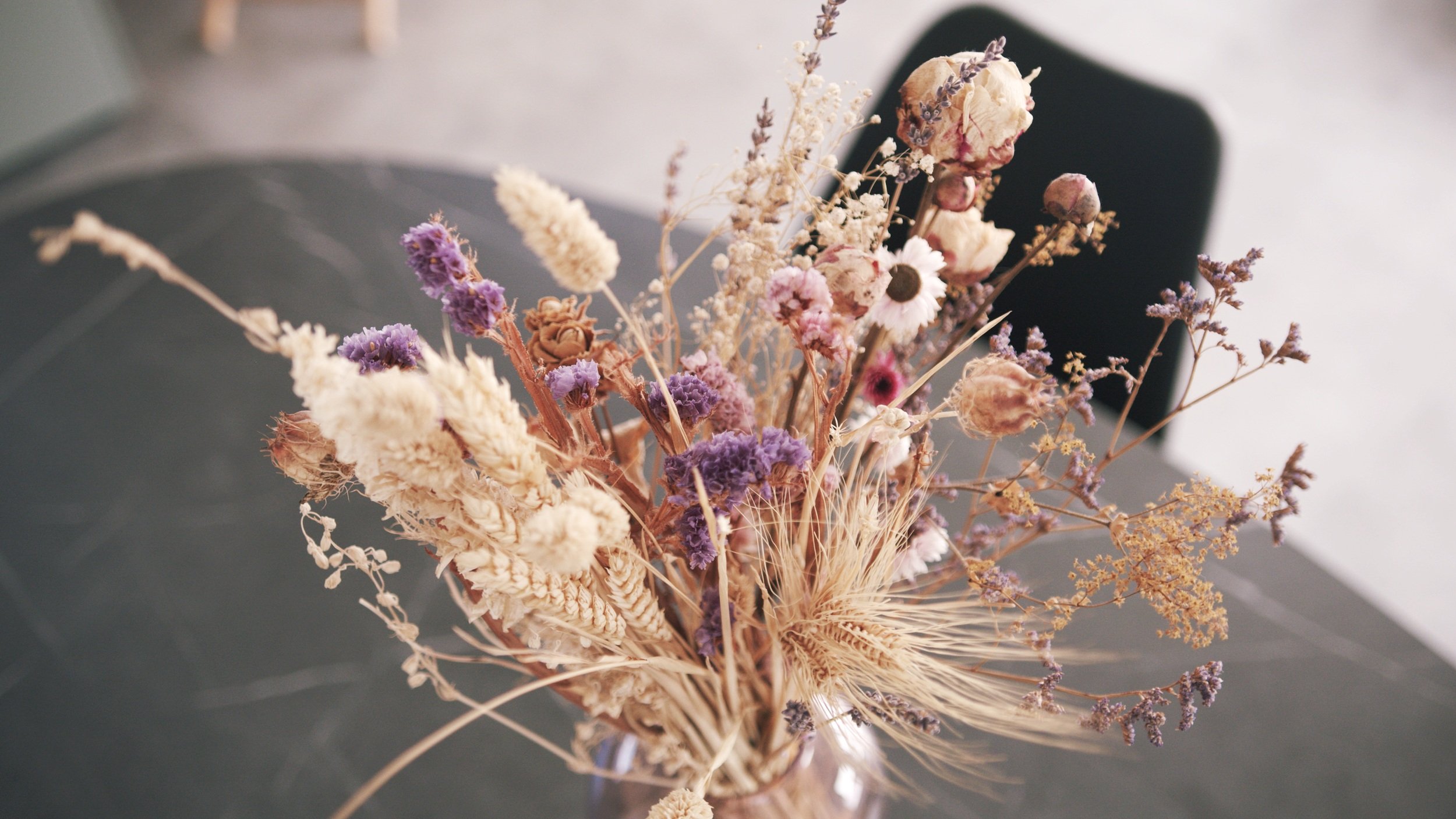 A bouquet of dried flowers and wheat in a vase on a dark table.