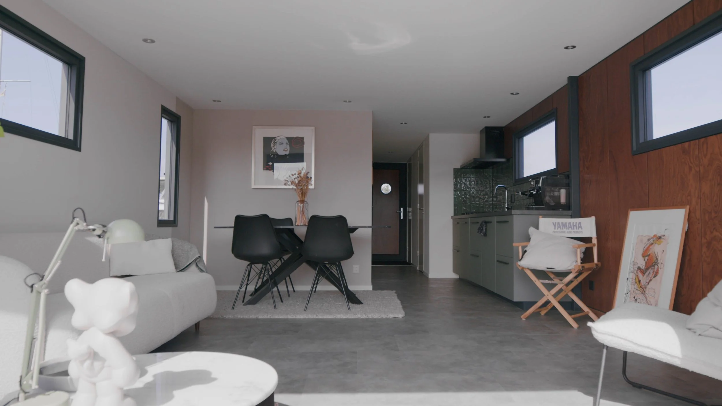 Modern interior with gray sofa, black dining chairs, kitchen area, and artwork on walls.