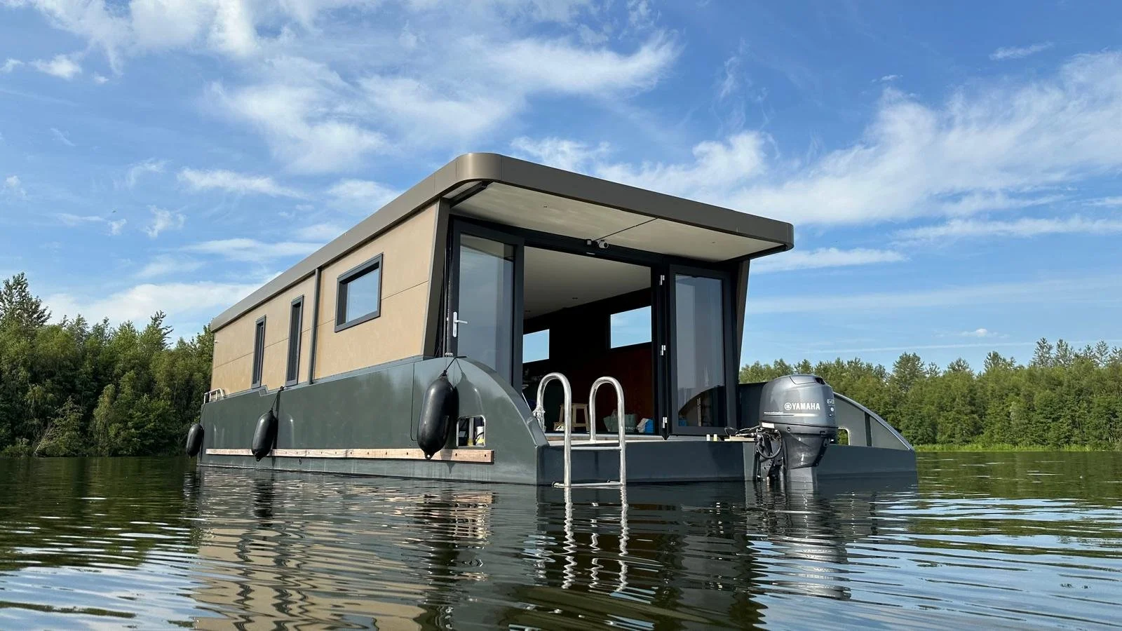 Modern houseboat on a lake with a forested background and blue sky