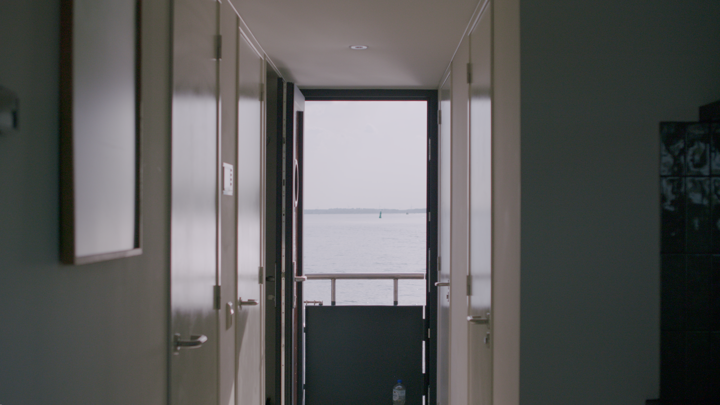 View of a corridor leading to a balcony with a water view in the distance.
