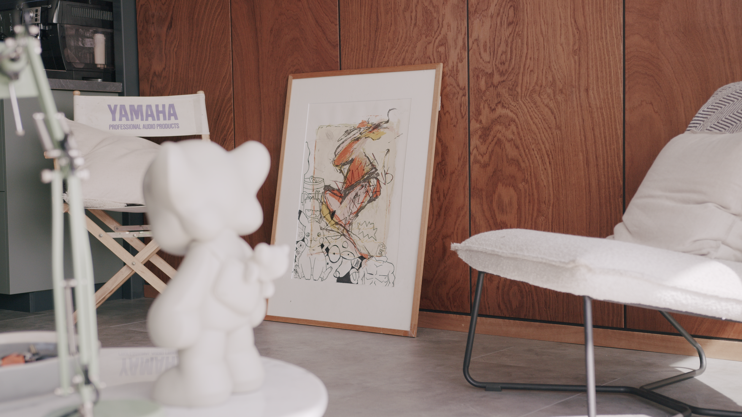 Interior space with modern art, wooden paneling, a Yamaha chair, a white decorative figure, a framed abstract painting, and a white cushioned chair.