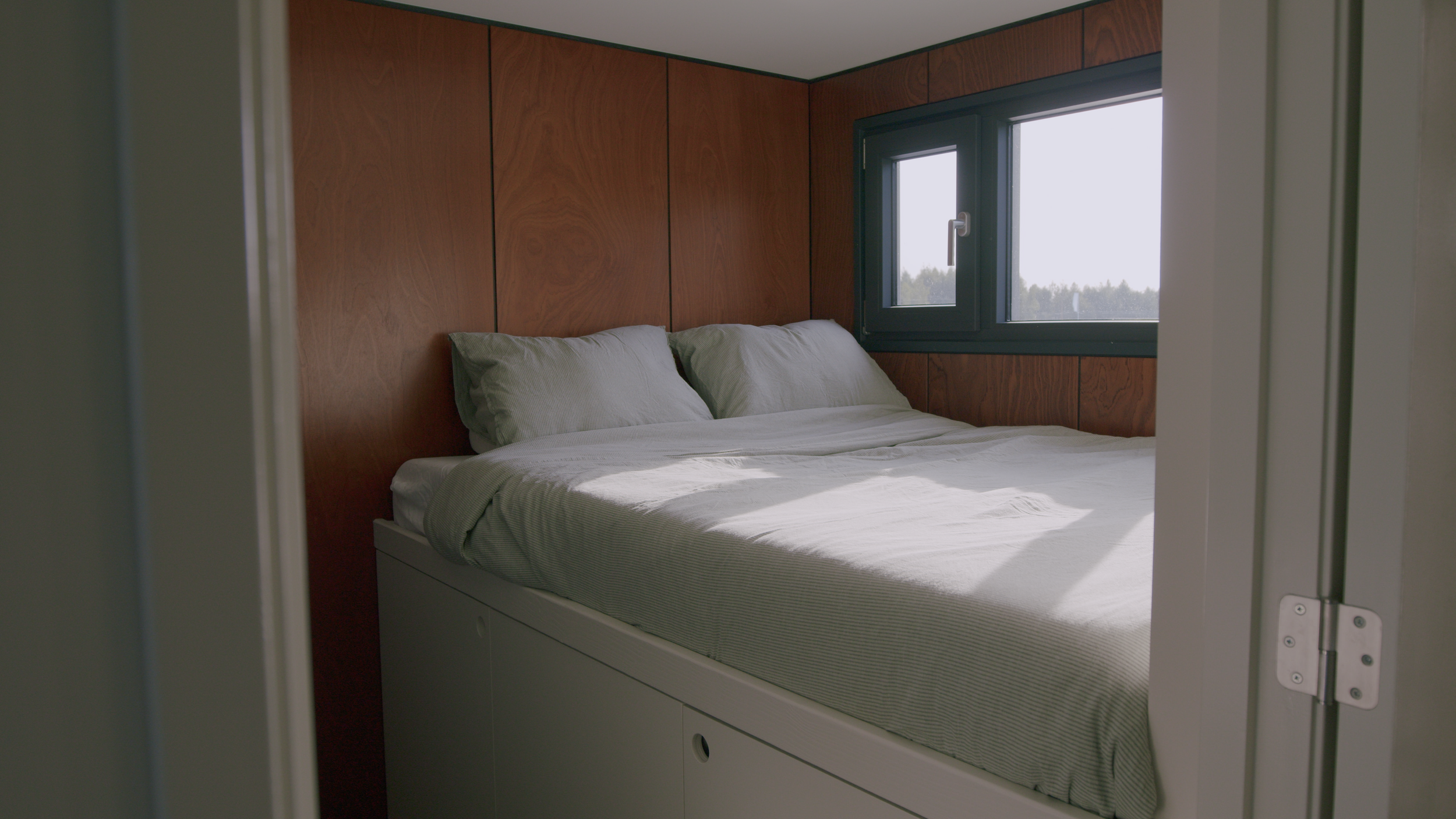 Small bedroom with a bed, wood-paneled walls, and a window.