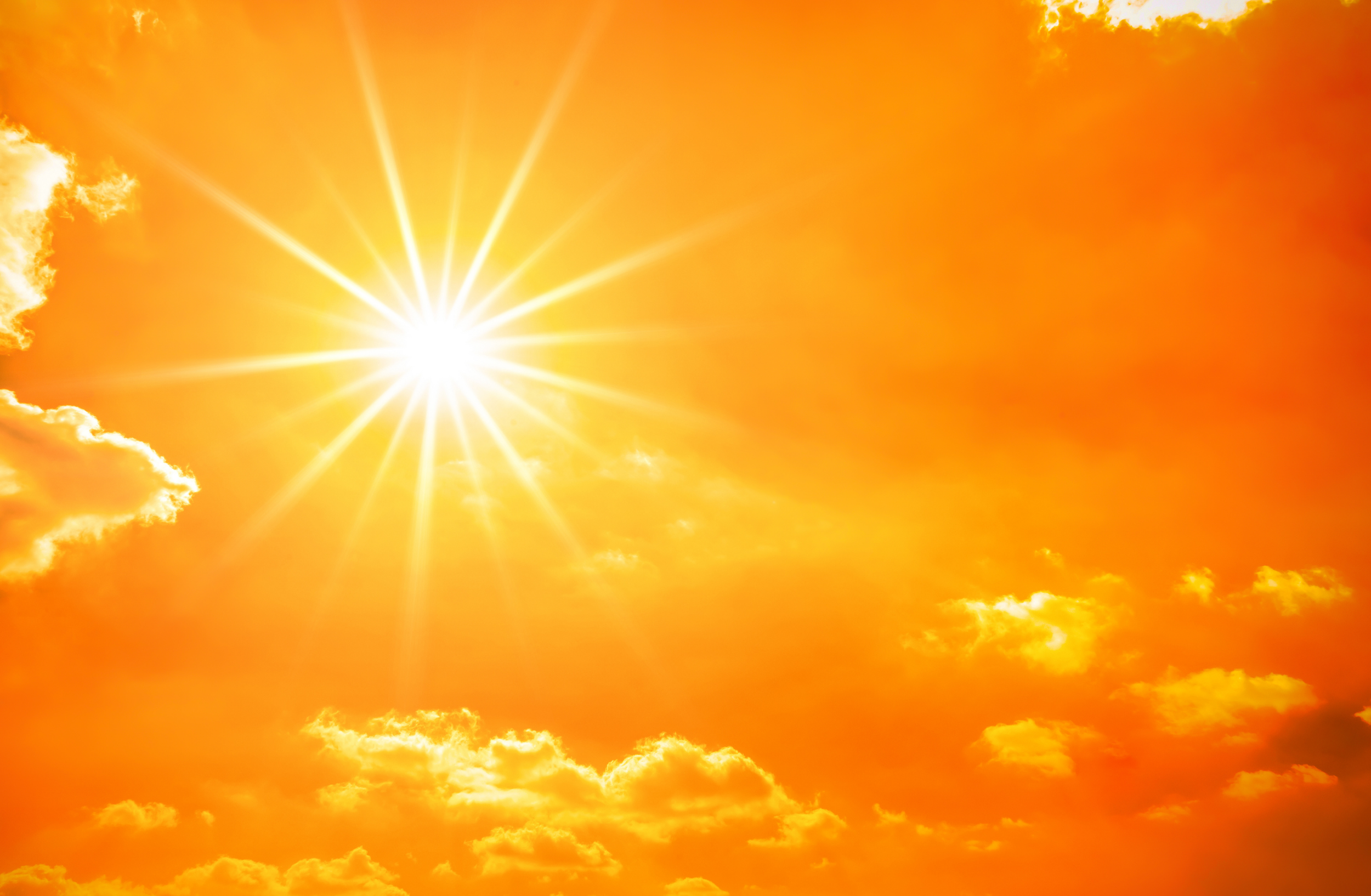 Bright sun shining through clouds in an orange sky.