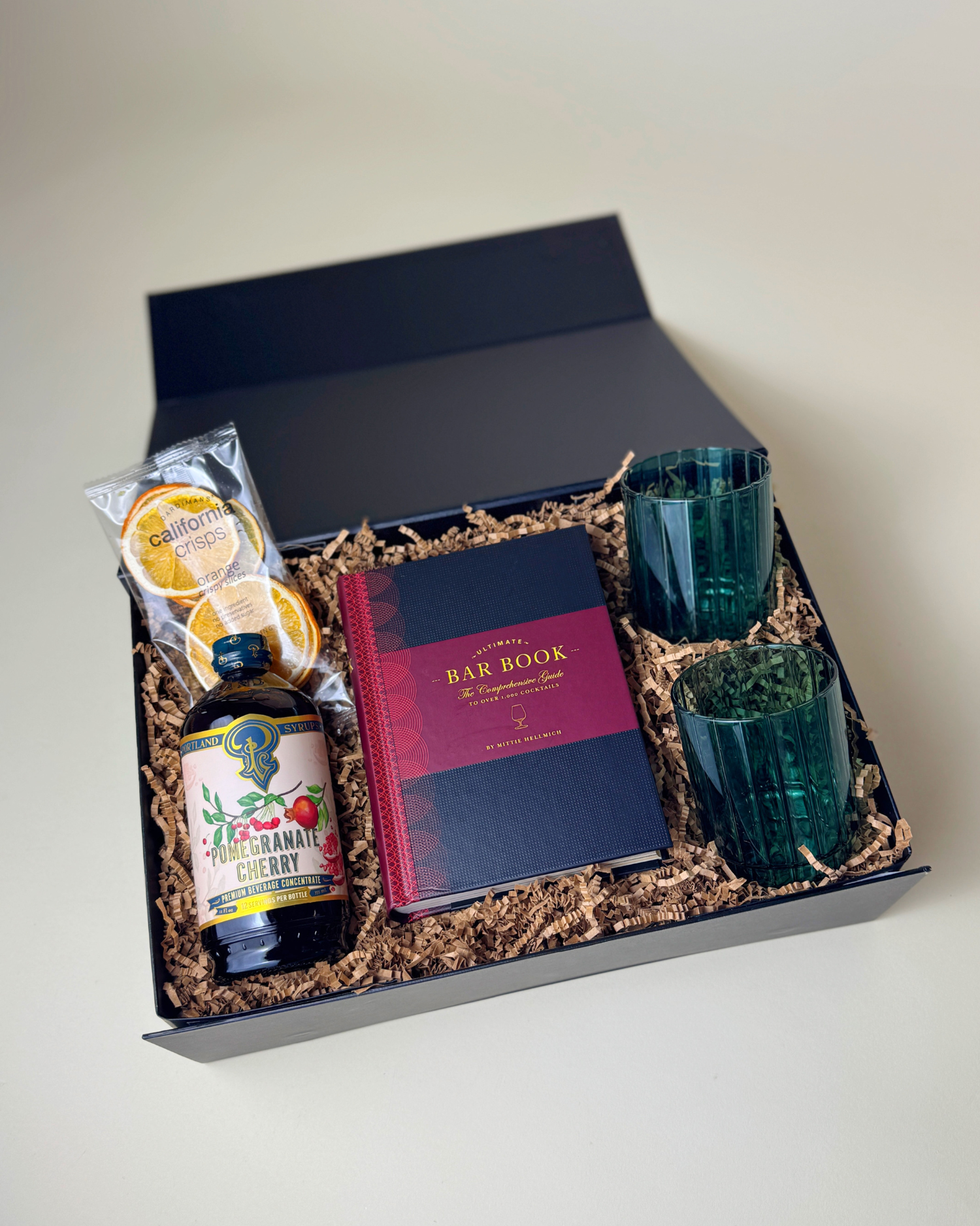 A flat lay of the items in the Holiday Spirits Gifts, including a mixer, cocktail book, dehydrated orange slices, and vintage-inspired glasses