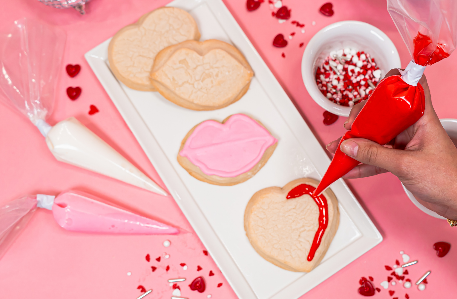 Hands decorating heart-shaped sugar cookies with icing and sprinkles at a corporate cookie decorating station in Austin.