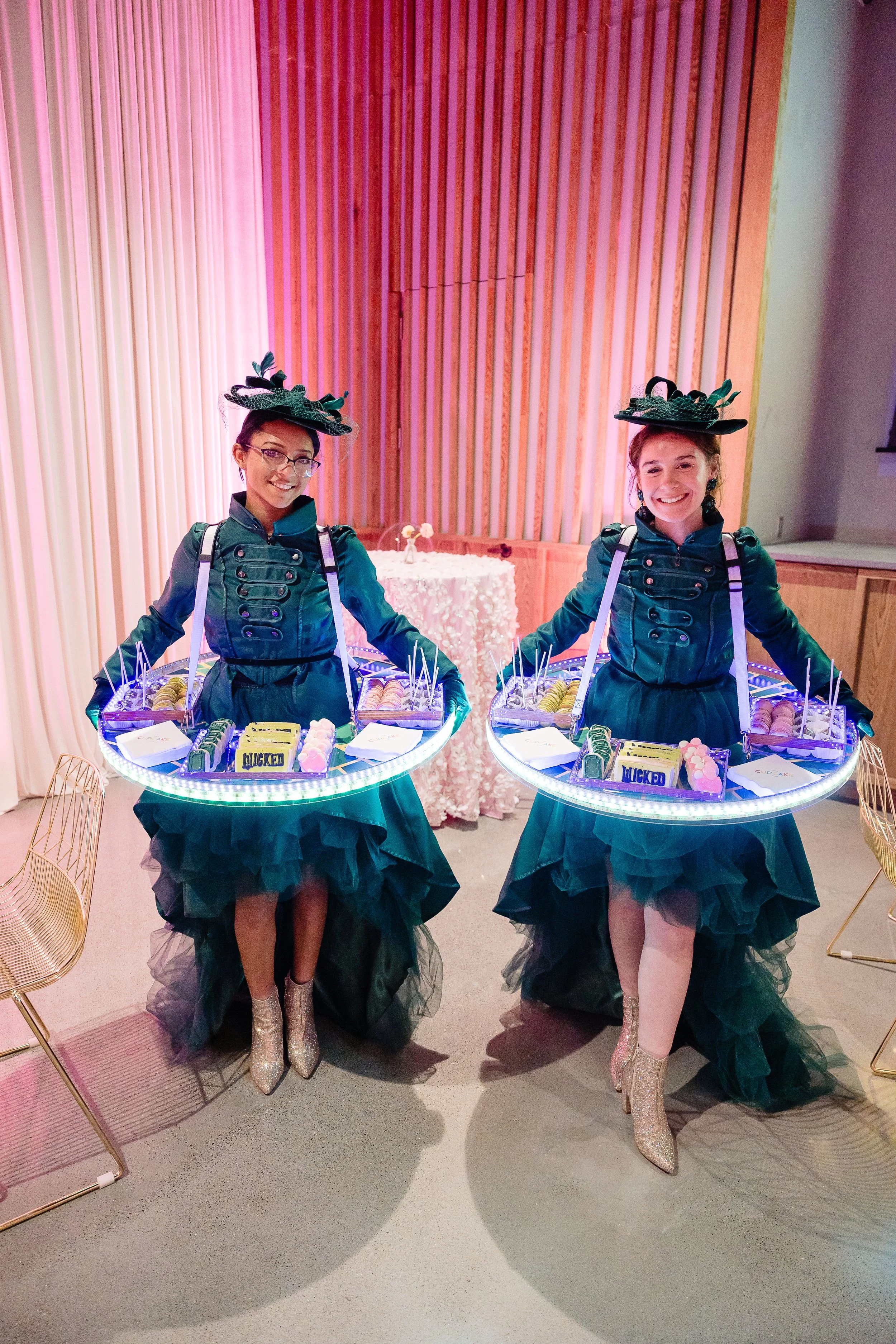Two costumed servers wearing dazzling glow orbit trays serving custom designed treats at a Wicked themed event in Austin, TX