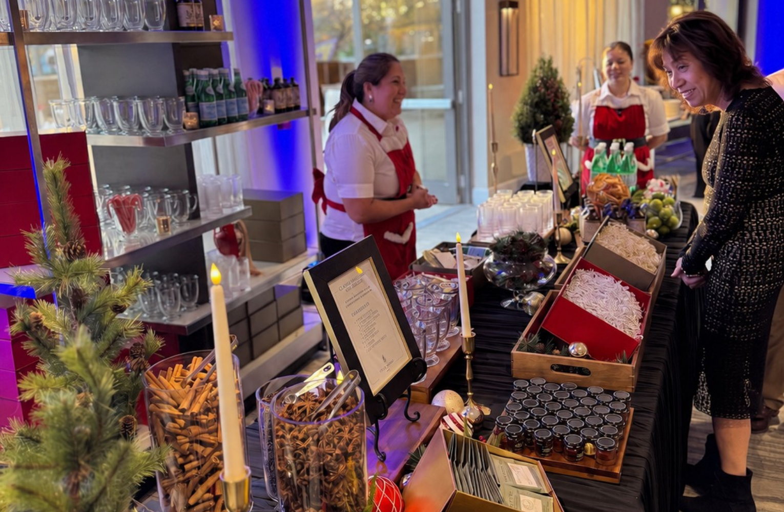 The Cupcake Bar staff assisting a Four Seasons resident at a holiday cocktail and mocktail gifting station with seasonal ingredients, gift boxes, and recipe displays.