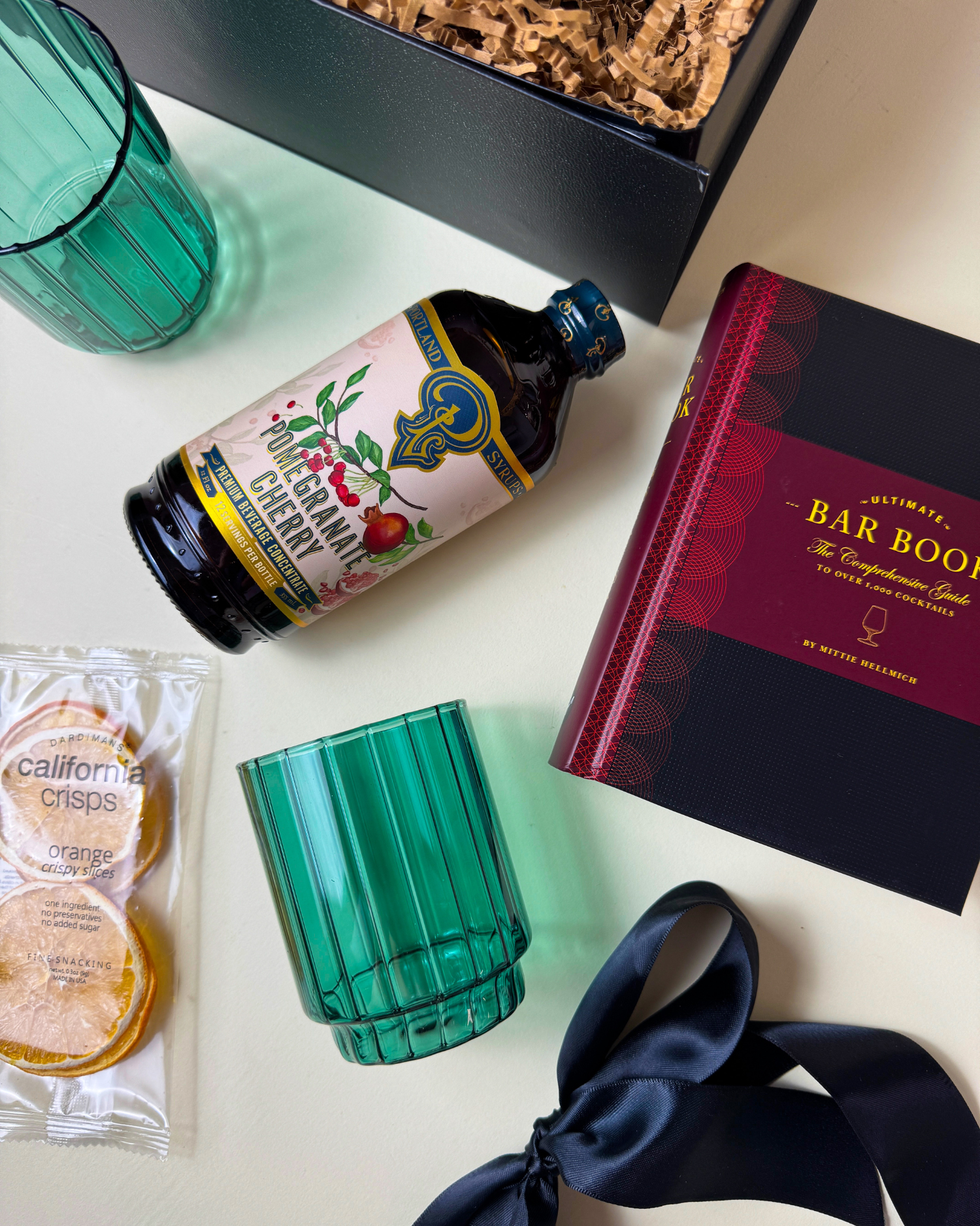 A flat lay of the items in the Holiday Spirits Gifts, including a mixer, cocktail book, dehydrated orange slices, and vintage-inspired glasses
