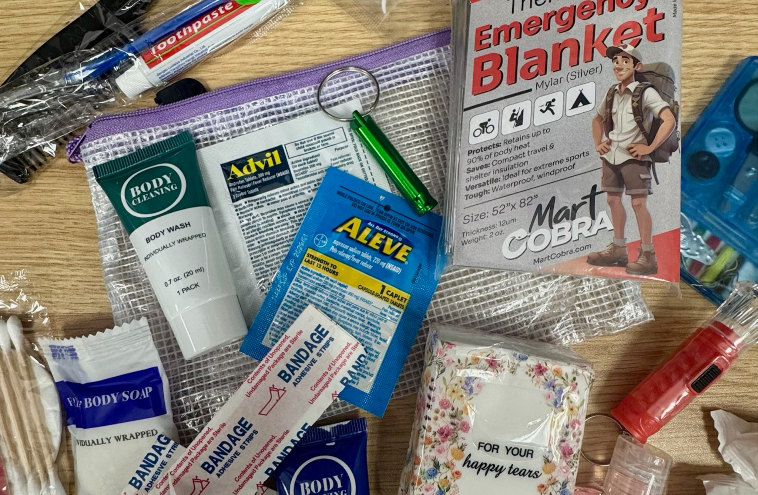 Assorted event emergency supplies, including bandages, pain reliever, an emergency blanket, toiletries, tissues, a flashlight, and a sewing kit arranged on a table.
