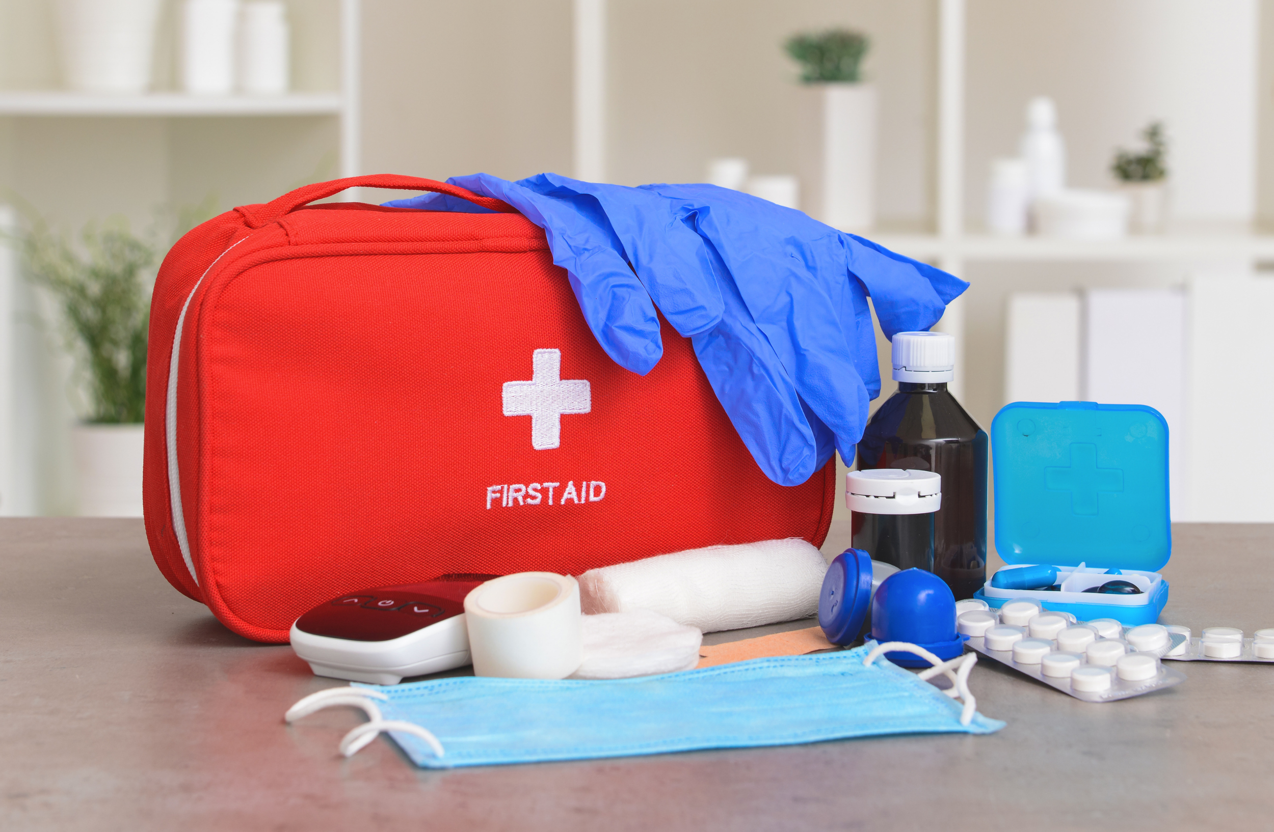 Red first aid kit surrounded by gloves, bandages, medicine bottles, masks, and other medical supplies.
