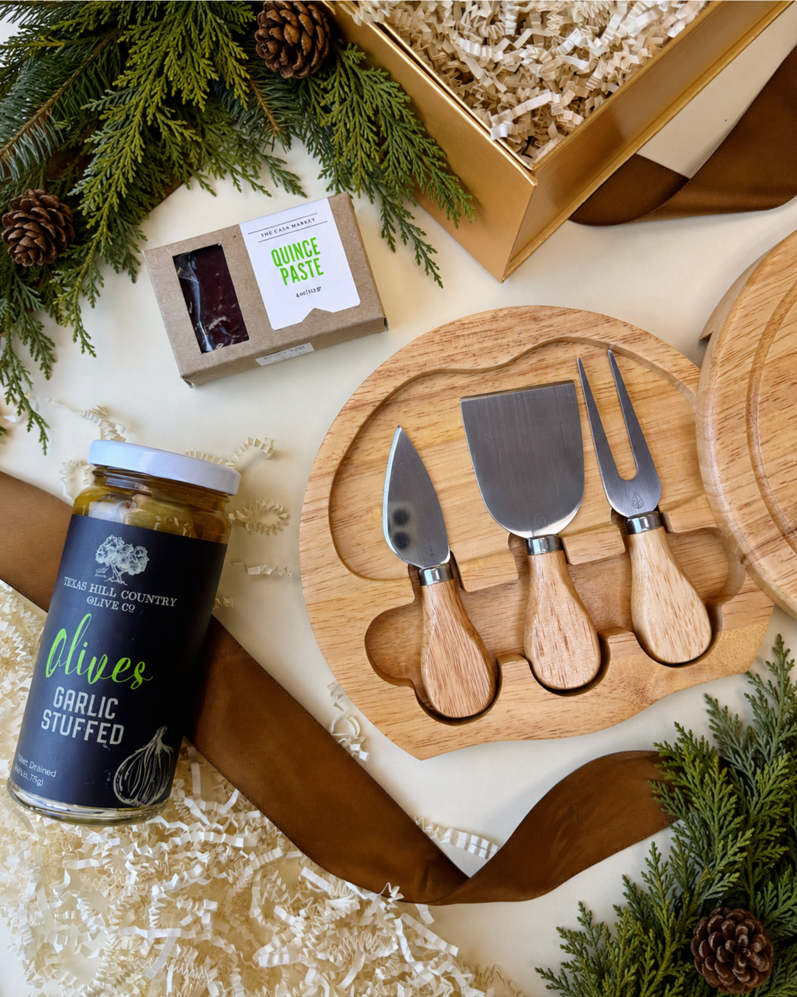 Close up of affordable charcuterie gift including a cheese board and knife set, gourmet table olives, and quince paste.